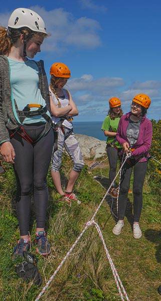 Four women are being instructed on how to correctly abseil, using the safety gear