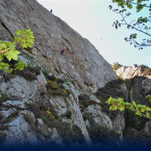 Woman abseiling down a large cliff face as a guilde supports above