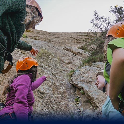 Four people point up and admire their achievement of descending a large cliff